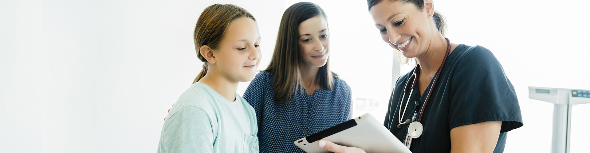 Ärztin zeigt einer Mutter und ihrer Tochter Untersuchungsergebnisse auf einem Tablet