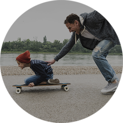 Bewegung fördern Vater schiebt Kind auf Skateboard an