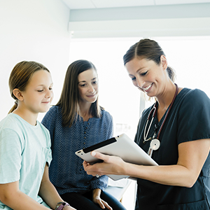 Ärztin zeigt einem Mädchen und ihrer Mutter Untersuchungsergebnisse auf einem Tablet