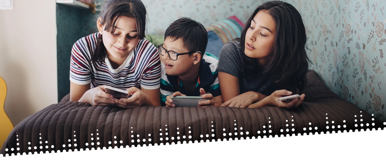 Zwei Mädchen und ein Junge liegen auf einem Bett und schauen auf ihre Handys Zwei Mädchen und ein Junge liegen auf einem Bett und schauen auf ihre Handys